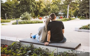 Ein junges Pärchen sitzt auf einer Bank im Kurpark. Drumherum sind schöne Blumenbeete angelegt. Leute spazieren im Kurpark.