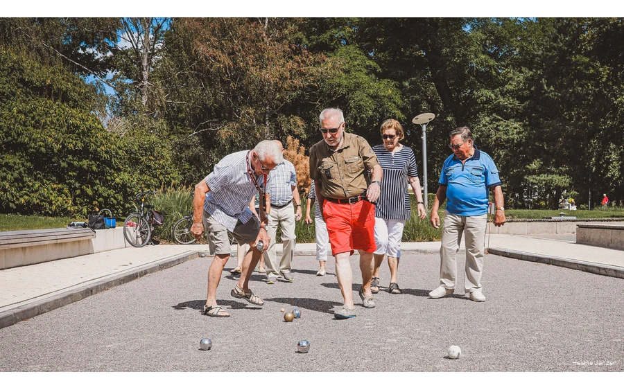 Eine Gruppe Boulespieler (4 Männer und 3 Frauen) auf dem Boulefeld im Kurpark, stehen um ihre geworfenen Boulekugeln herum und erörtern die Ergebnisse.