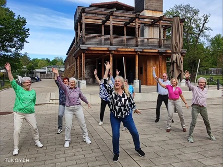 Eine Gruppe unterschiedlicher Menschen tanzt im Kurpark Bad Sassendorf. Alle haben Spaß dabei und lachen.